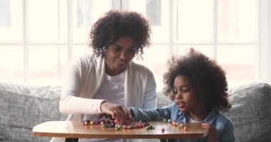 Mixed race mum babysitter teaching kid daughter making necklace
