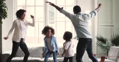 Happy african couple dancing with preschool children in living room