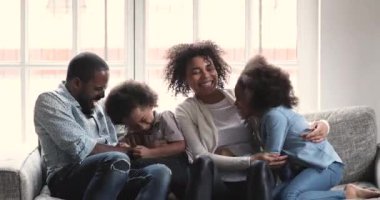 Cheerful affectionate african family tickling laughing hugging cuddling on sofa