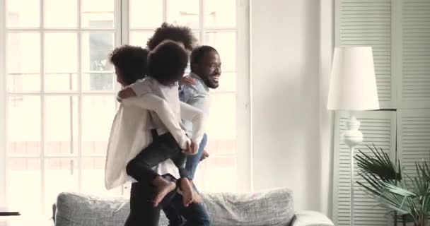 Gelukkig actieve Afrikaanse ouders meeliften kinderen spelen in de woonkamer — Stockvideo