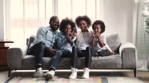 African parents and children watching video using phone on couch — Stockvideo