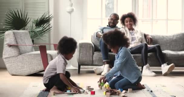 Afrikaanse kinderen spelen op de vloer terwijl ouders ontspannen op de bank — Stockvideo