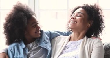 Happy african mum and daughter cuddling having fun on sofa