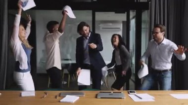 Happy multiracial colleagues dancing in office, throwing papers in air.