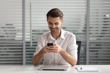 İş yerinde cep telefonuyla mesajlaşan gülümseyen erkek işçi.