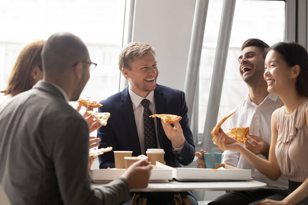 Happy multiethnic colleagues chat enjoying pizza in office