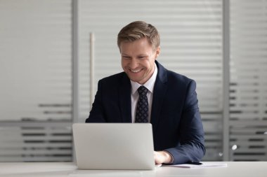 Gülümseyen işadamı ofiste dizüstü bilgisayarla çalışıyor.