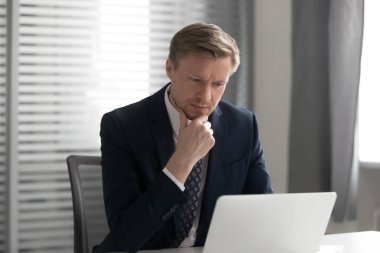 Düşünceli erkek çalışanın dizüstü bilgisayarı kullanarak iş fikrini değerlendirmesi