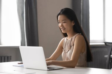 Milenyum Asyalı kadın ofiste dizüstü bilgisayarla çalışmakla meşgul.