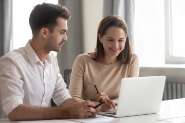 Smiling diverse colleagues work together using laptop