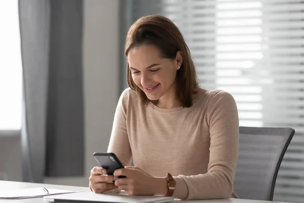 Mujer de negocios sonriente usando mensajería de teléfono celular en el lugar de trabajo —  Fotos de Stock