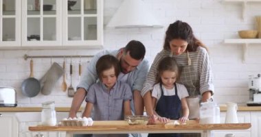 Smiling couple teaching children siblings flattening dough with rolling pins.