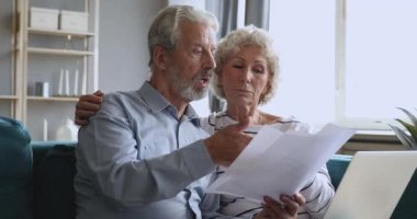 Focused older man discussing monthly expenses at home with wife.