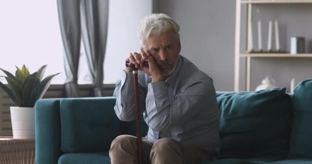 Thoughtful middle aged man sitting on couch relying on stick. — Stockvideo