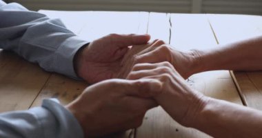 Mature retired family couple holding hands together on table.