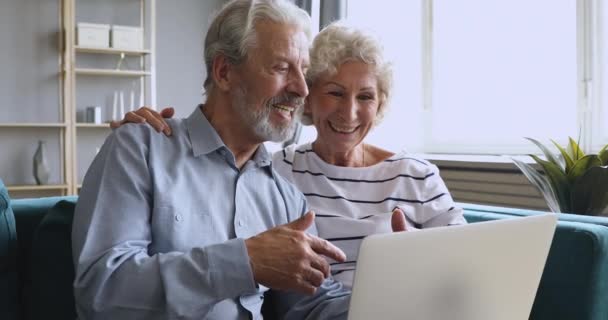 Smiling 60s woman cuddling pleasant husband, explaining computer software. — Stockvideo