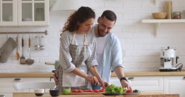 Young man cuddling smiling attractive wife in apron preparing food.
