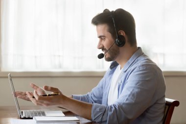 Male worker in headset consult clients on laptop online