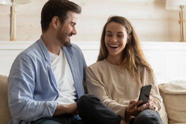 Happy young couple have fun using cellphone at home