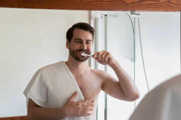 Young man brushing teeth after shower in home bathroom — ストック写真