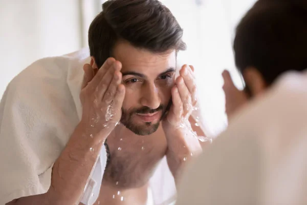 Young man look in mirror washing face in bathroom — Stock Photo, Image