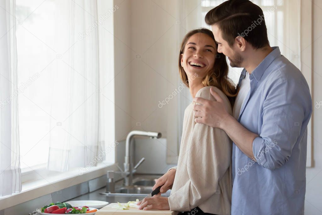 Smiling young couple hug in kitchen cooking together