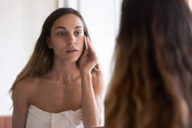 Young woman look in mirror perform skincare routine in bath