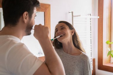 Happy millennial couple brush teeth in bath together