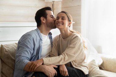 Loving man kiss girlfriend relaxing on couch together