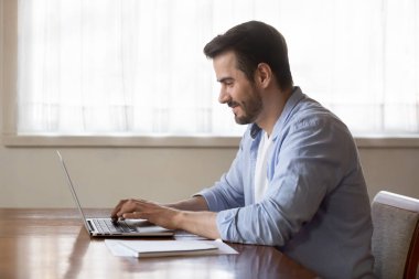 Smiling man using modern laptop typing message