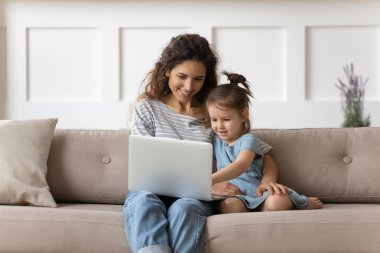 Smiling young mother teaching little daughter using computer applications.