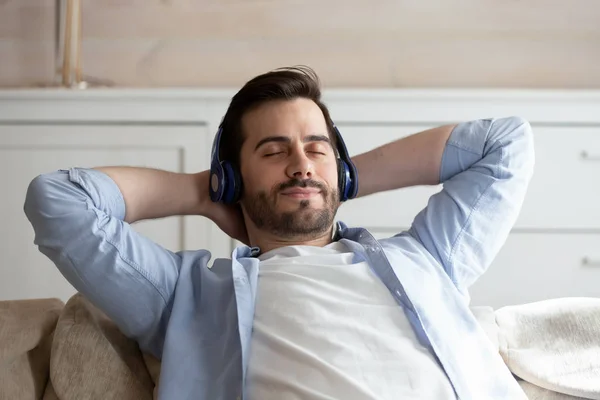Calm young man listen to music relaxing on couch