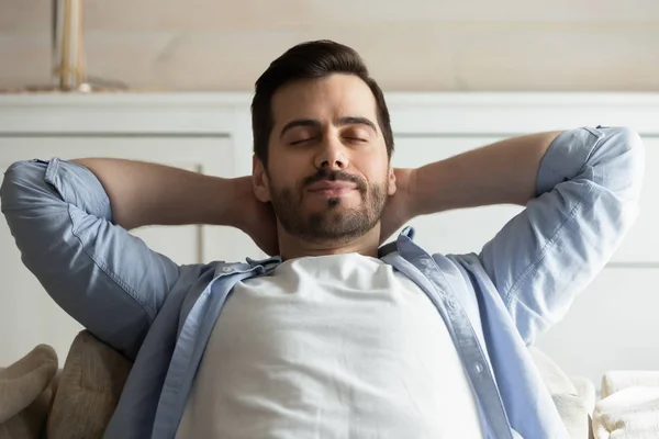 Calm millennial man relaxing with eyes closed on cozy couch