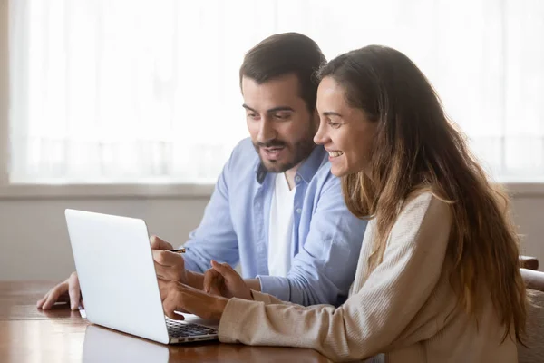 Lachend jong stel zitten aan tafel met behulp van laptop samen — Stockfoto