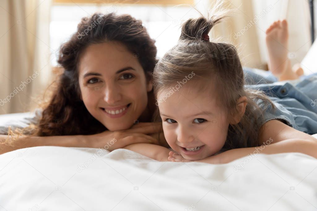 Happy adorable woman resting on bed with little preschool daughter.