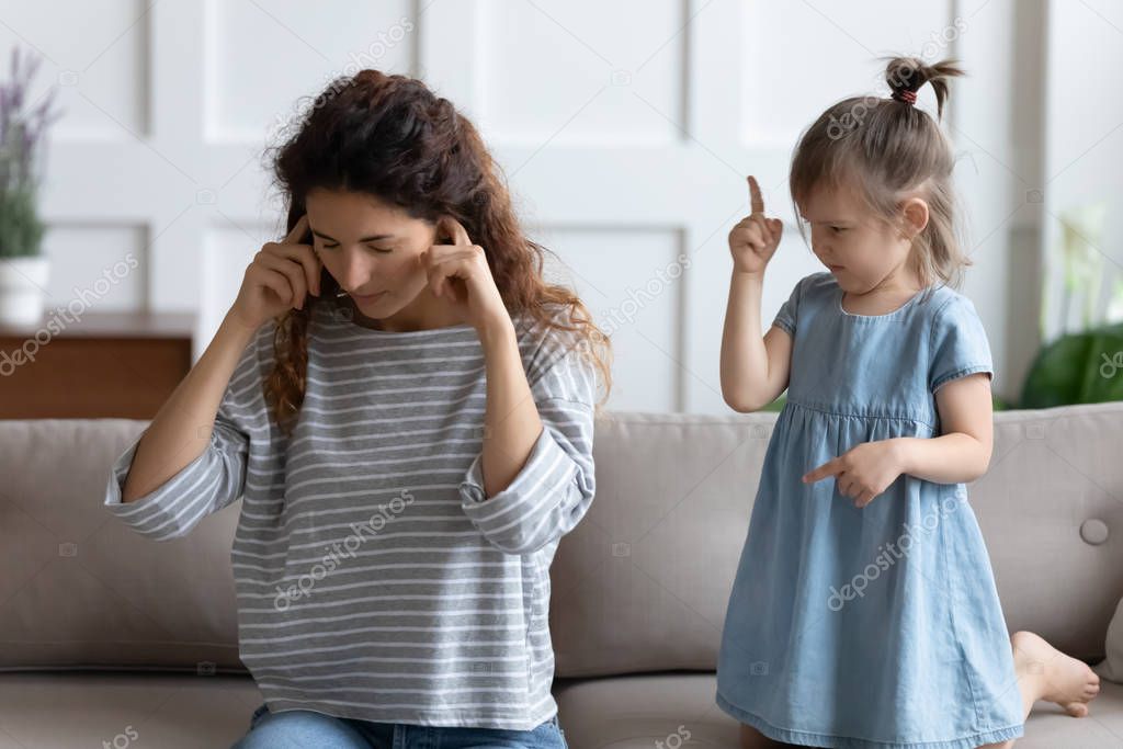 Stressed young mother covering ears, annoyed by bad daughters behavior.