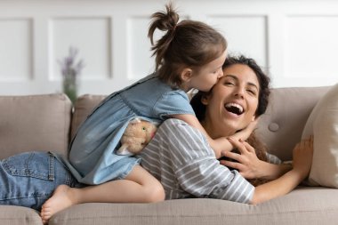 Playful small preschool daughter kissing mothers cheek.