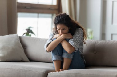 Stressed young woman embracing knees, sitting alone on couch.