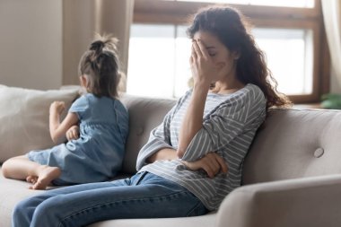 Unhappy mother touching forehead, feeling tired of bad daughters behavior.