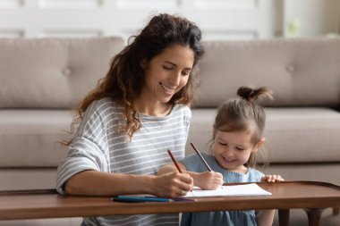 Joyful young mommy drawing cute pictures with adorable daughter.
