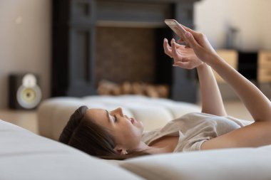 Millennial girl resting on sofa using smartphone gadget