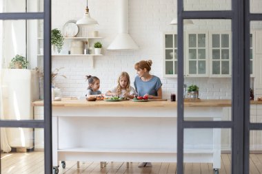 Young mother cooking at home with small daughters
