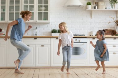 Overjoyed young mum and little daughter dance in kitchen