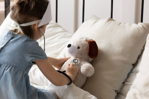 Little preschool girl playing doctor patient with toy in bedroom.