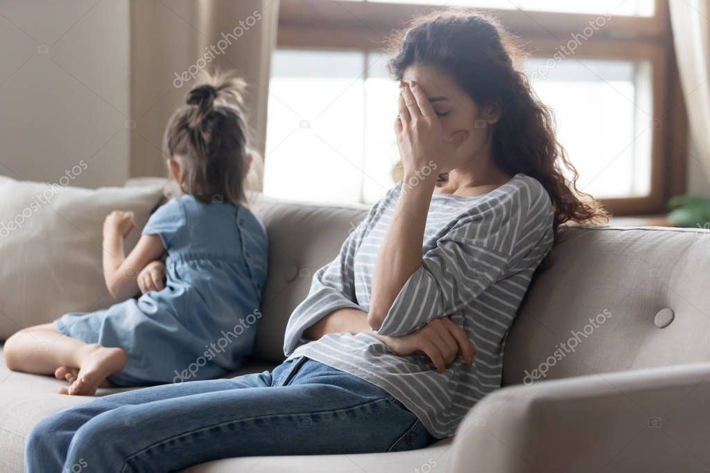 Unhappy mother touching forehead, feeling tired of bad daughters behavior.