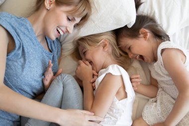 Overjoyed mother playing with little daughters in bedroom