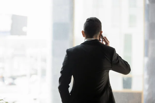 Rear view businessman in formal suit talking on phone indoors — 图库照片