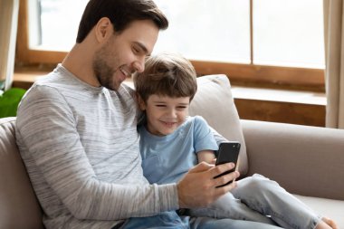 Happy young father cuddling little son, showing funny mobile applications.