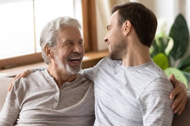 Happy mature old man cuddling shoulders of grownup son.