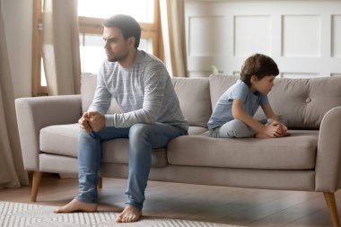 Annoyed young father sitting back to back with little son.